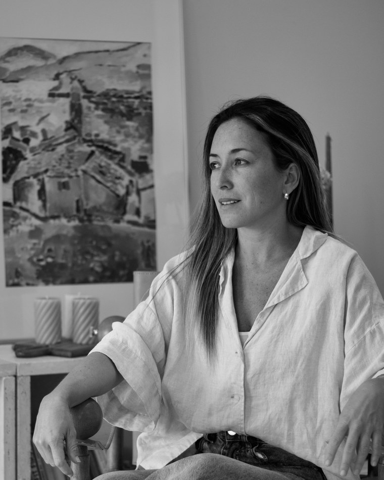 Black and white portrait of Mohana Aspillaga, seated, with artwork in the background
