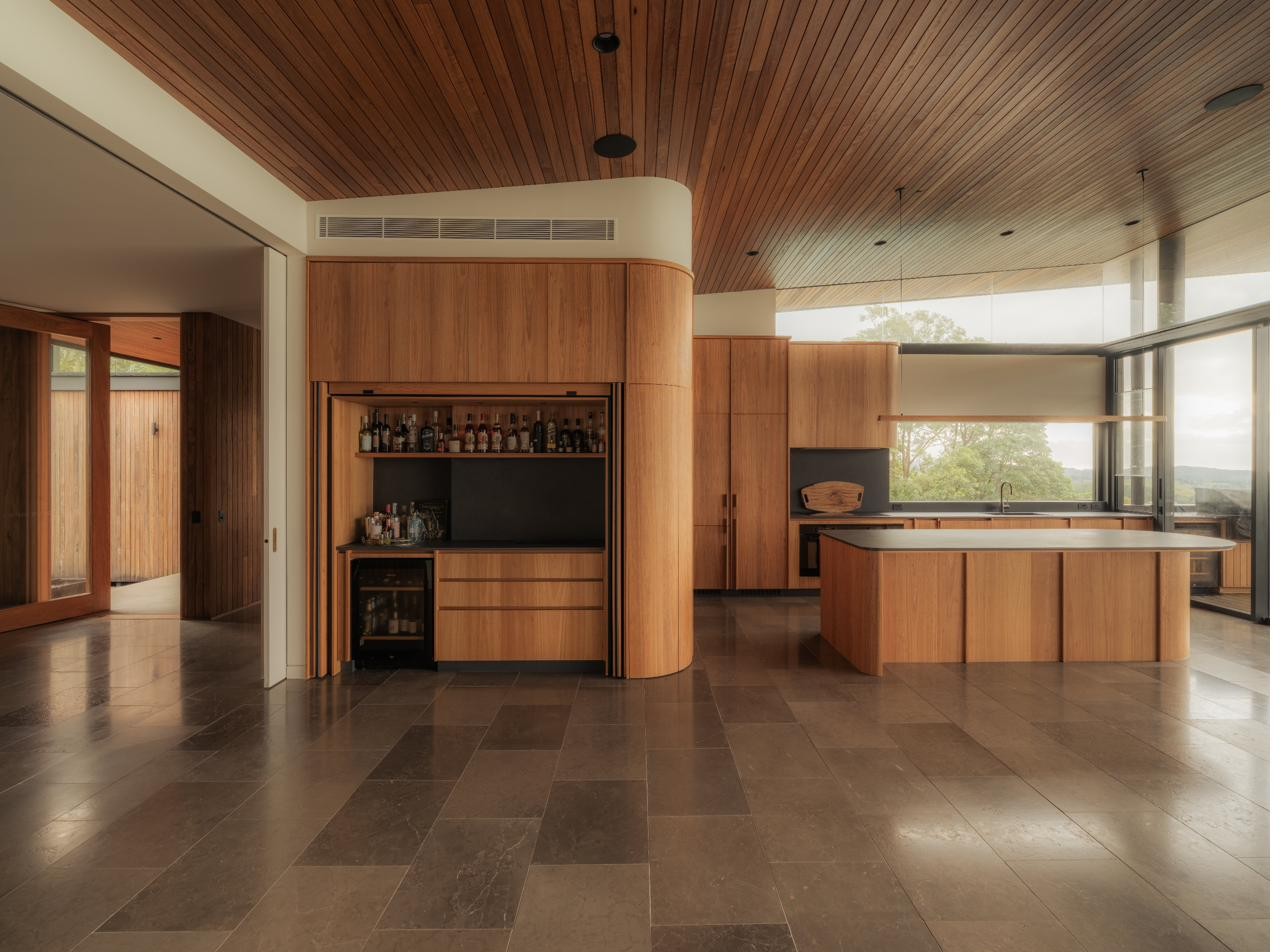 Kitchen and living space with curved timber joinery, Newrybar Residence